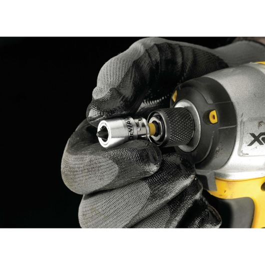 Gloved hand attaching a DEWALT socket to a power tool against a black background.