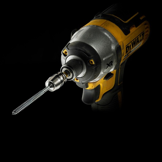 Close-up of a DEWALT power drill with a screwdriver bit attached, shown against a black background.