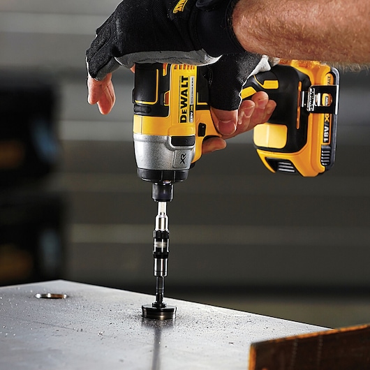 A person wearing gloves uses a DEWALT cordless drill with an attachment to drill a hole in a metal surface.