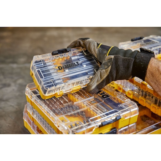 Gloved hand holding a DEWALT drill bit case with stacked yellow and clear cases in the background.