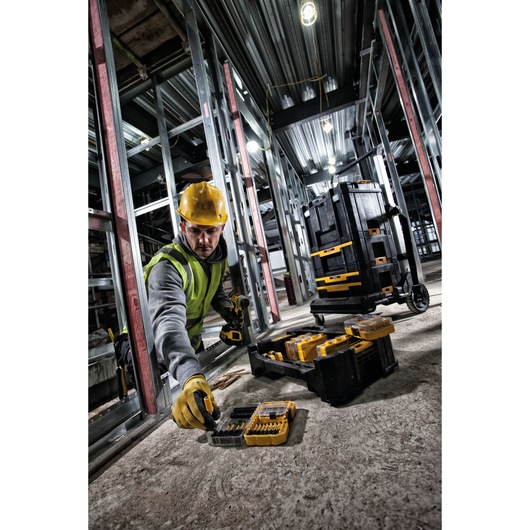 A construction worker in a high-visibility vest and hard hat uses DEWALT tool bit sets on a concrete floor at an industrial