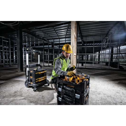 Person wearing a yellow hard hat and safety vest organizing DEWALT toolboxes and accessories in a partially constructed