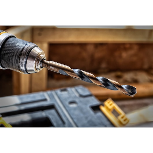 Close-up of a DEWALT drill bit attached to a drill, with construction materials and tools visible in the background.