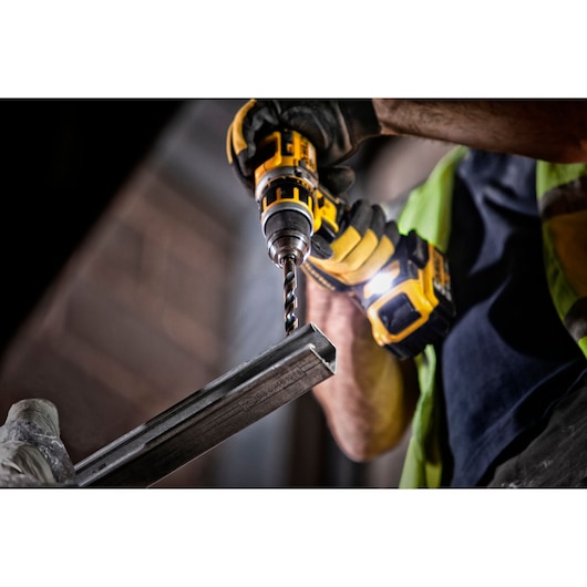 A person wearing protective gloves uses a DEWALT cordless drill to drill into a piece of metal.