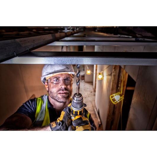 A construction worker wearing safety gear is using a DEWALT drill to create a hole in a metal beam inside a building under