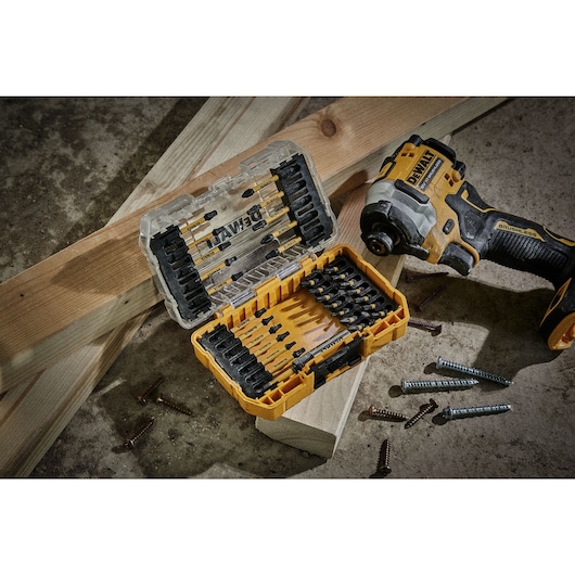 DEWALT drill bit set in yellow case, impact driver, screws, and wooden beams placed on a concrete surface.