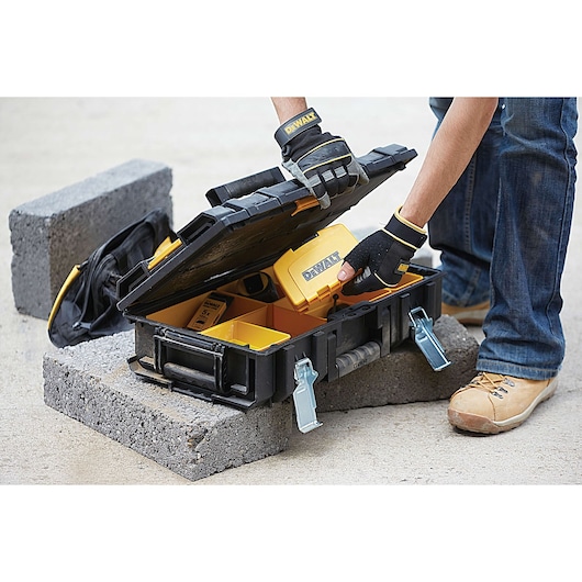 Person with gloves opens DEWALT toolbox on concrete blocks, holding a yellow tool inside.