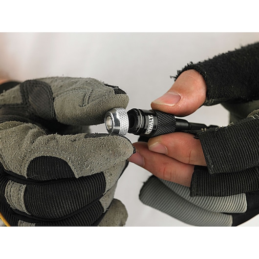 A close-up of gloved hands holding a DEWALT DT71514 tool accessory, possibly a bit holder or adapter, commonly used in photography or construction tasks.