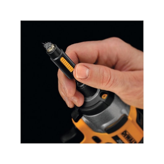 Close-up of a hand holding a DEWALT tool with a wire brush accessory attached, showing detail of the tool's grip and yellow accents.