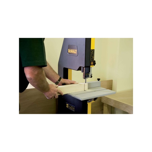 A person using a DEWALT band saw to cut a piece of wood in a workshop.