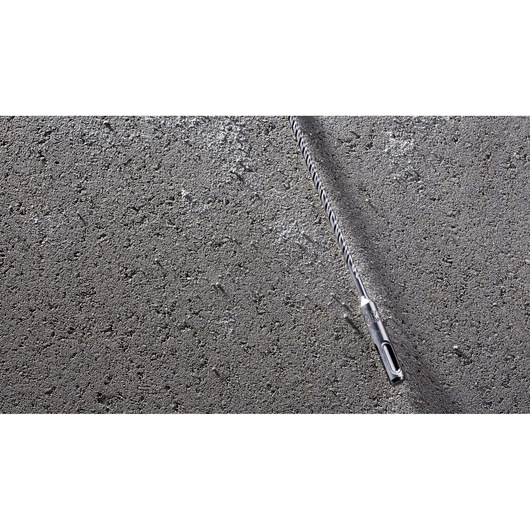 A DEWALT DT8909 long spiral drill bit is placed diagonally on a rough concrete surface.