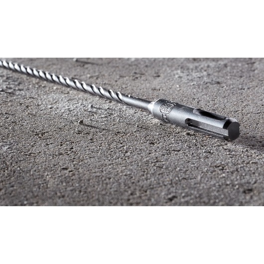 A close-up image of a DEWALT DT8909 masonry drill bit with an SDS connection, lying on a rough concrete surface.