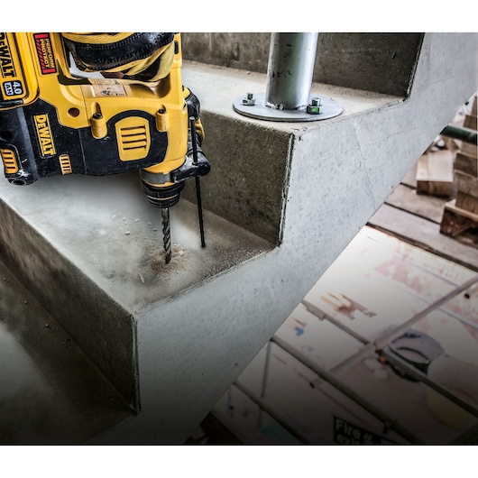 A DEWALT cordless rotary hammer drill is being used to drill into a concrete staircase on a construction site.