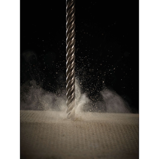 Close-up of a DEWALT DT8932 spiral drill bit penetrating a textured surface, creating a burst of dust and debris.