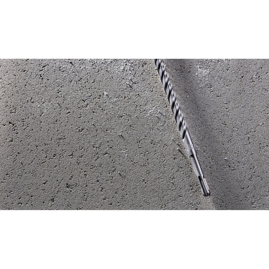 A close-up image of a DEWALT DT8935 masonry drill bit partially inserted into a grey concrete surface.