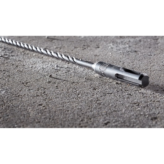 A DEWALT metal drill bit with a spiral design lying on a rough concrete surface.