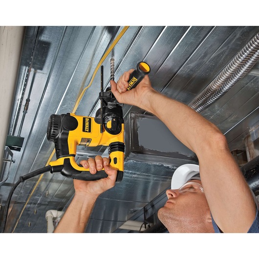 A person using a DEWALT corded power drill with a side handle to drill into a metal ceiling. The person's face is blurred for privacy.