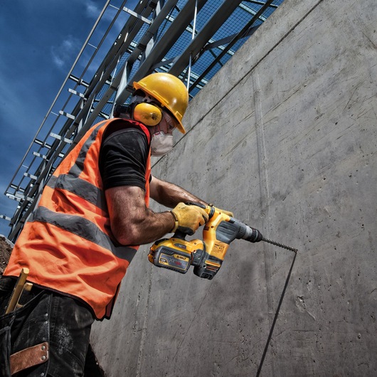A construction worker wearing safety gear uses a DEWALT DT9580 power tool to drill into a concrete wall at a building site.
