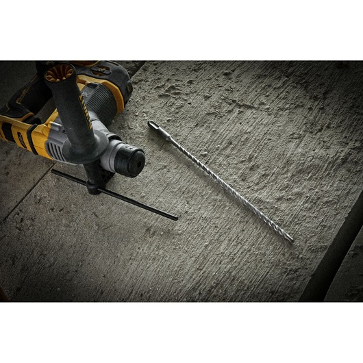 A DEWALT rotary hammer drill and a long masonry drill bit on a textured concrete surface.