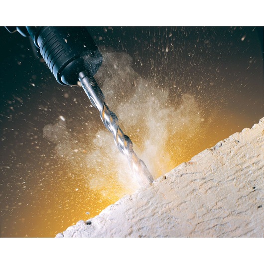 Close-up of a DEWALT drill bit drilling into a concrete surface, with dust and debris flying.