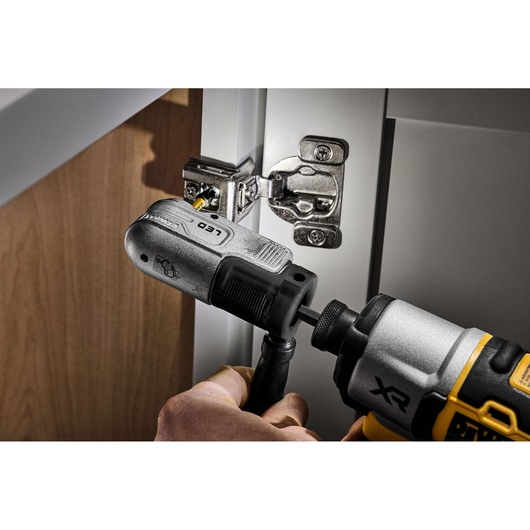 DEWALT attachment on drill driving screw into cabinet hinge in close-up view.