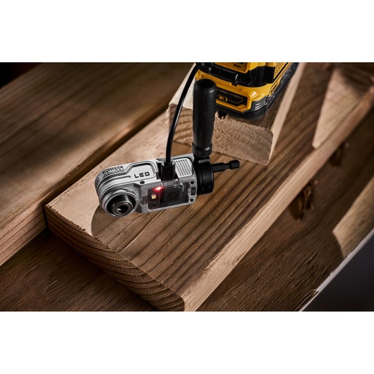 DEWALT LED camera tool attached to a yellow power drill, placed on wooden planks in a workshop setting.