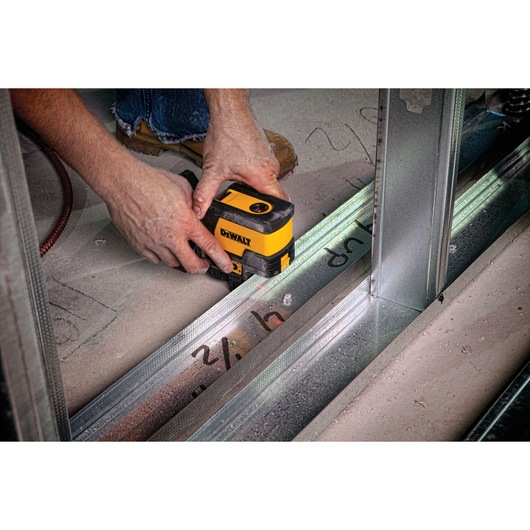 A person is using a DEWALT laser level device to measure and align metal framing on a construction site floor.