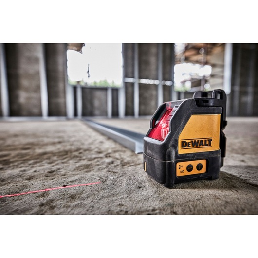 A DEWALT DW088K self-leveling cross line laser level placed on a construction site floor, projecting a visible red laser line used for alignment tasks.