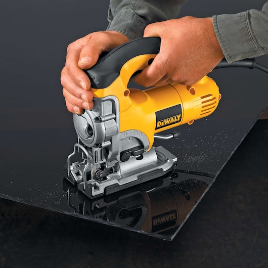 A person using a yellow and black DEWALT jigsaw (model DW331K) to cut a black material sheet.