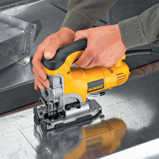 A person using a yellow DEWALT jigsaw (model DW331K) to cut a rectangular shape in a metallic sheet.