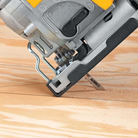 Close-up view of a DEWALT jigsaw cutting through a wooden board, showing the base and blade in action.