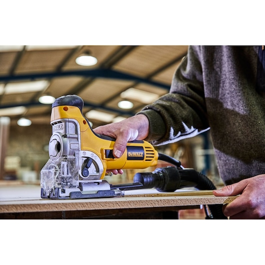 A person using a yellow DEWALT jigsaw to cut a piece of wood in a workshop setting.