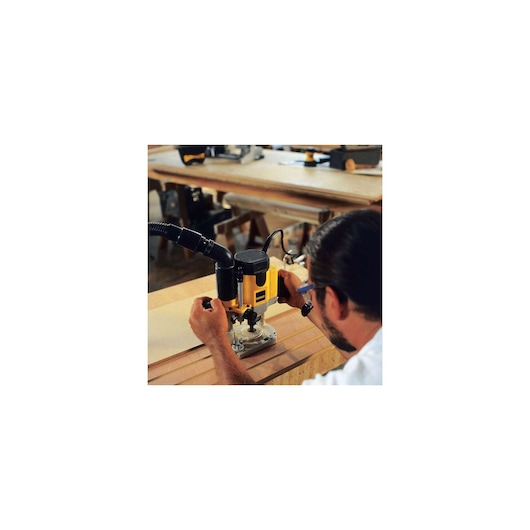 A person using a DEWALT DW621 router tool to cut grooves in a piece of wood on a workbench in a workshop.