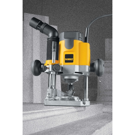 A DEWALT DW621 plunge router, featuring a yellow and black design, two handles, and a dust extraction attachment, shown in a workshop environment.
