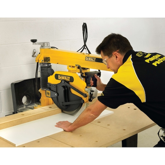 Person cutting wood with a DEWALT DW729KN radial arm saw in a workshop.