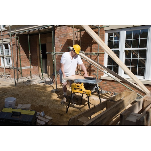 Worker using a DEWALT DW743N saw outdoors at a construction site with wooden planks and scaffolding nearby.