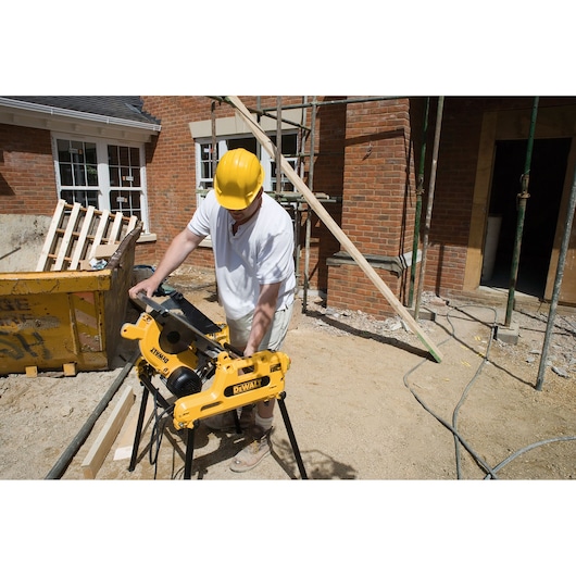 Person uses DEWALT DW743N saw on construction site outdoors near brick building.