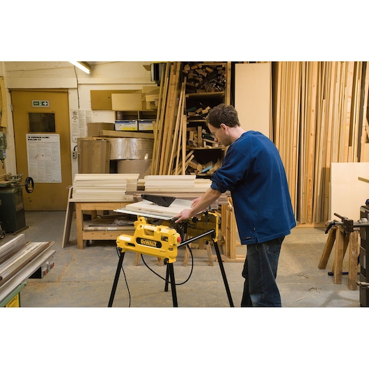 Person using DEWALT DW743N saw in a workshop with wooden boards and tools around.