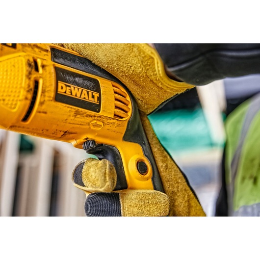 Close-up of a gloved hand holding a yellow DEWALT electric drill at a construction site.