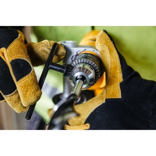 Close-up view of gloved hands adjusting the chuck of a yellow electric drill with a key, preparing the tool for use.