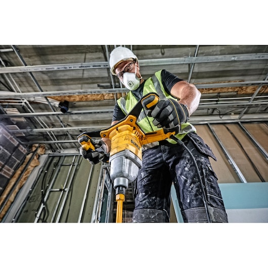 A construction worker wearing a safety vest, gloves, and a helmet is operating a DEWALT DWD241 electric mixer drill inside a