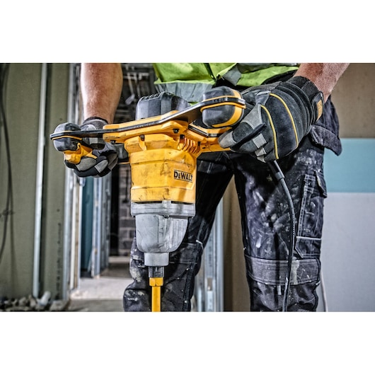 A person wearing work gloves and dark work pants uses a yellow DEWALT electric drill mixer in a construction environment.