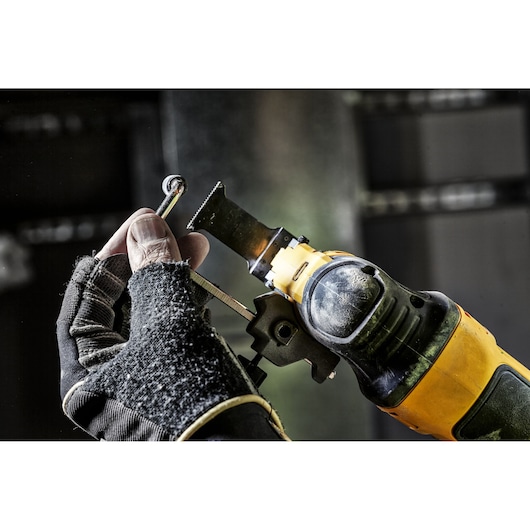 A close-up of a gloved hand using a yellow and black DEWALT oscillating multi-tool to cut a small metal object.