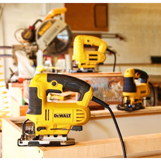 A close-up image of a DEWALT DWE349 jigsaw placed on a wooden workbench, with other DEWALT power tools visible in the background inside a workshop.
