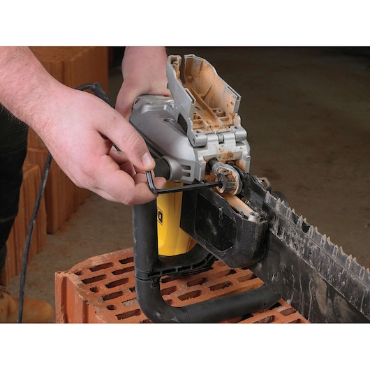 Person uses a hex key to adjust a DEWALT electric masonry saw placed on a brick.