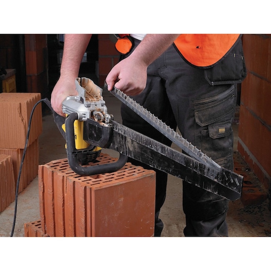 Person uses a DEWALT electric masonry saw to cut a large clay brick on a construction site.