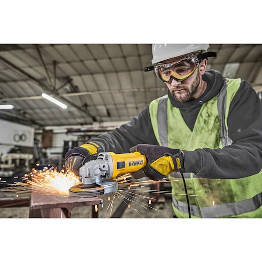 A worker in a safety vest and gloves uses a yellow DEWALT angle grinder, SKU DWE4036, to cut metal, creating sparks in an