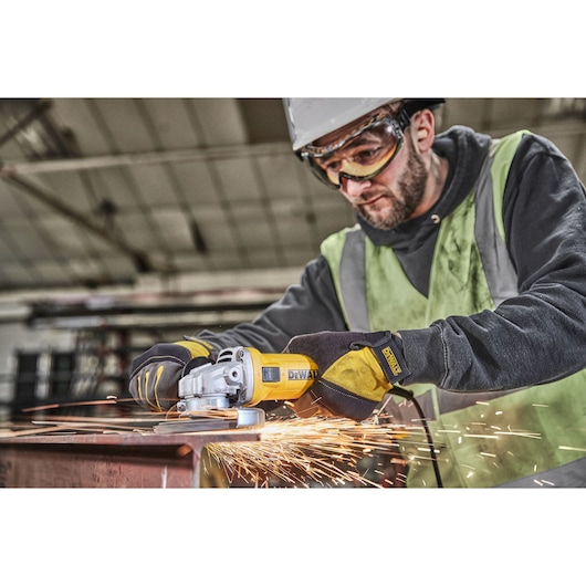 A person wearing safety gear operates a yellow DEWALT angle grinder, generating sparks while grinding metal in an industrial