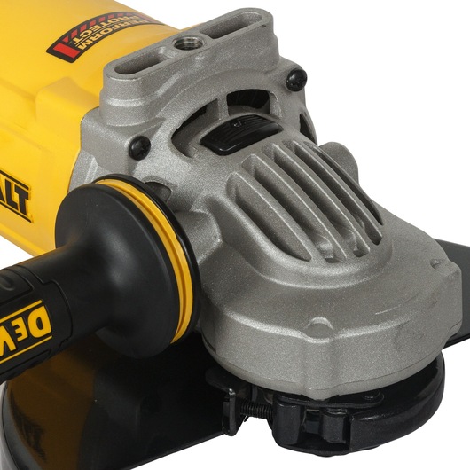 Close-up view of a DEWALT angle grinder, showing its metallic gear housing, black handle with yellow accents, and part of the grinding disc.