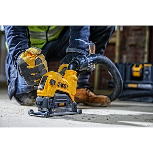 A person wearing work gloves is operating a DEWALT electric tool connected to a hose, working on a concrete floor. DEWALT tool cases are visible in the background.